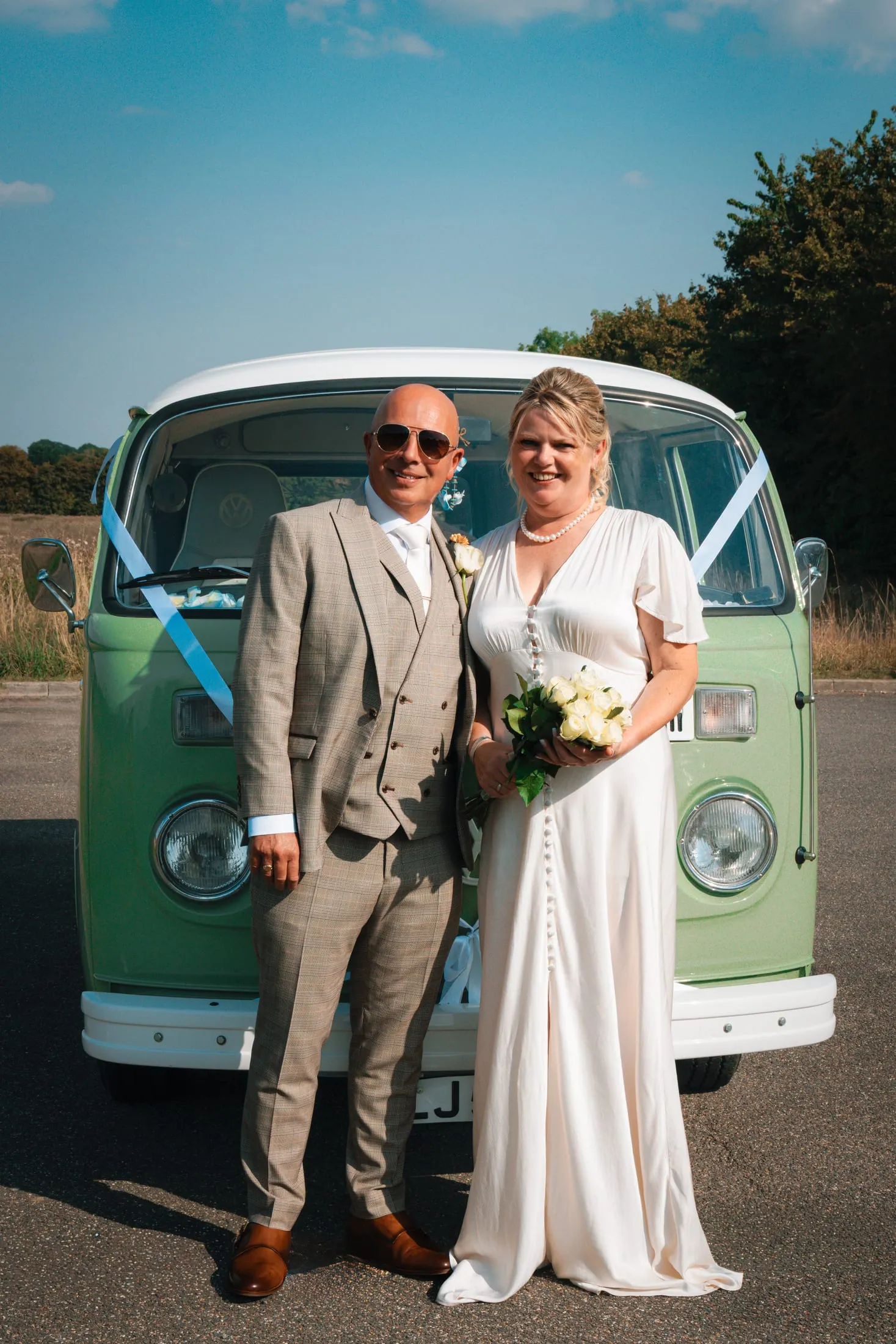Bride and groom in front of a vintage green VW camper van, the bride holding white roses