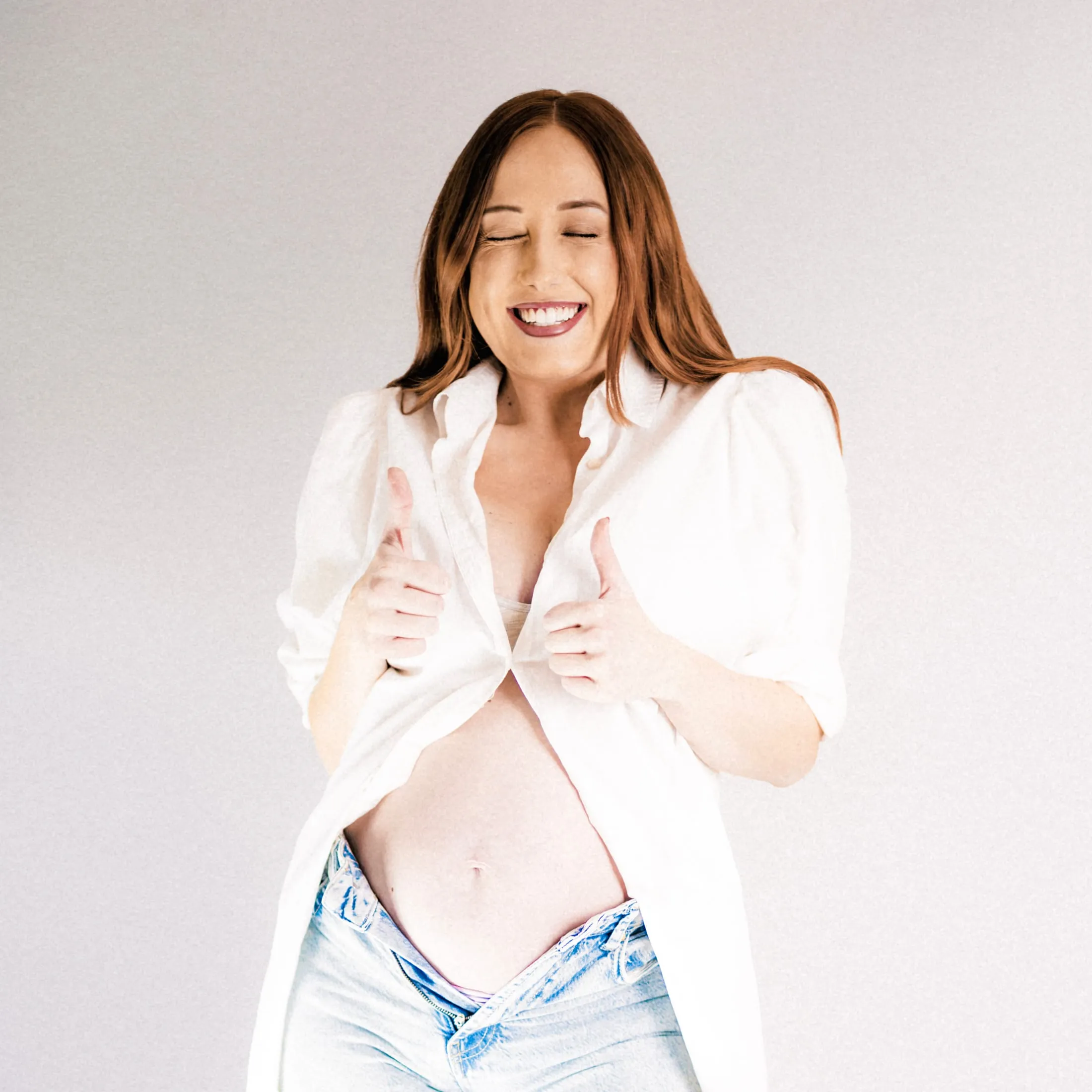 Laughing expectant mother in an open white shirt over her bump