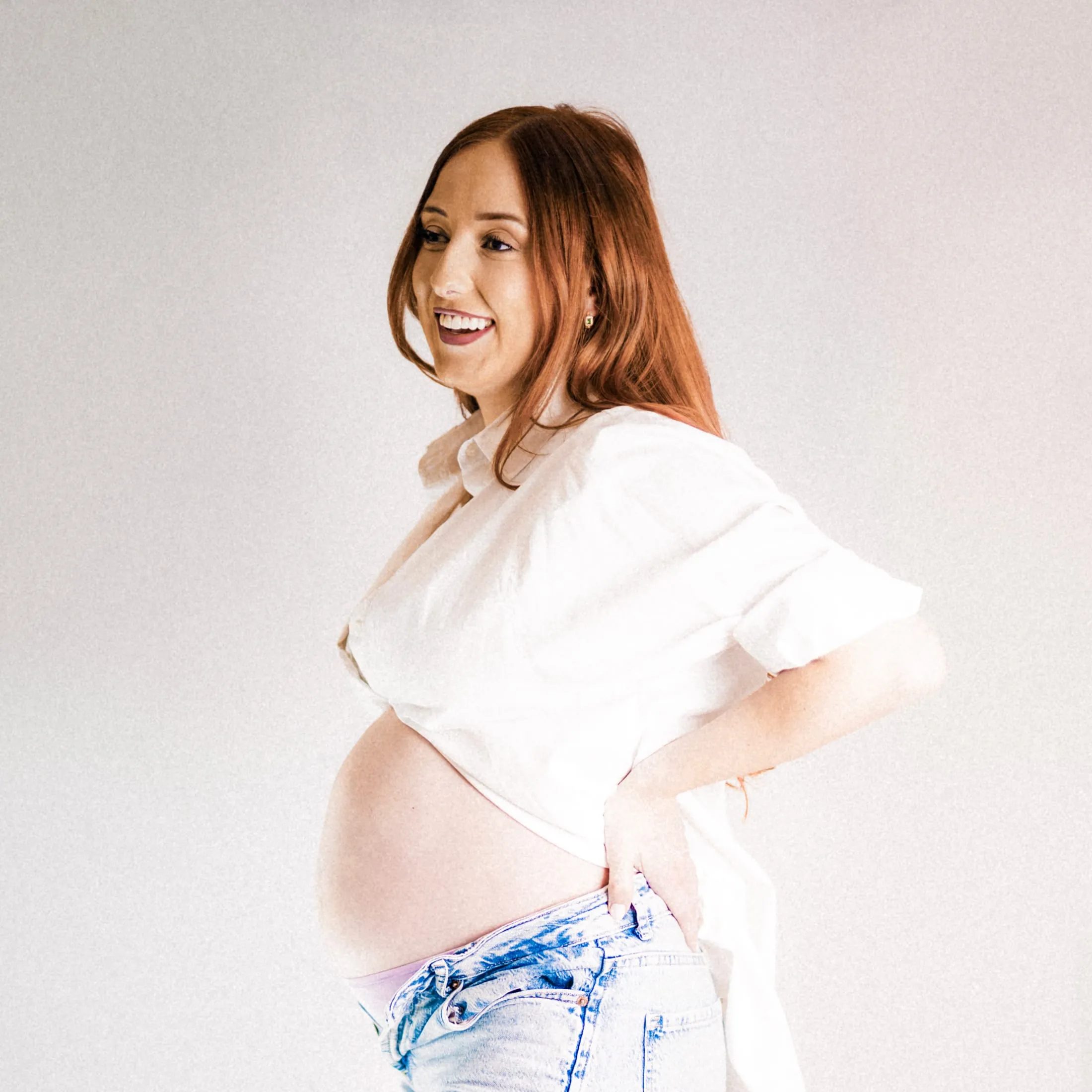 Expectant mother in profile with a hand on her hip, in soft studio light