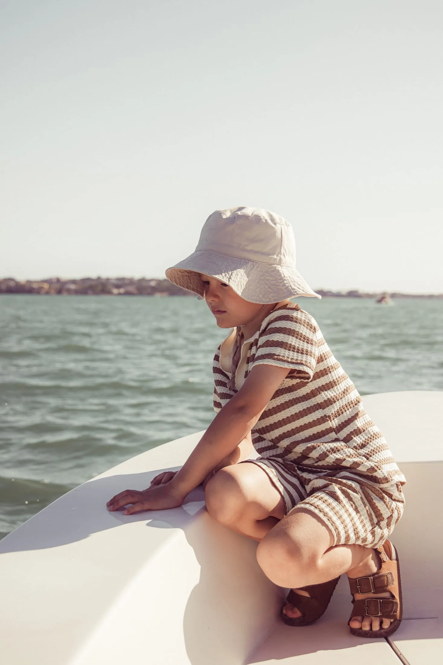 Child in a sun hat on the bow of a boat, looking out over the water
