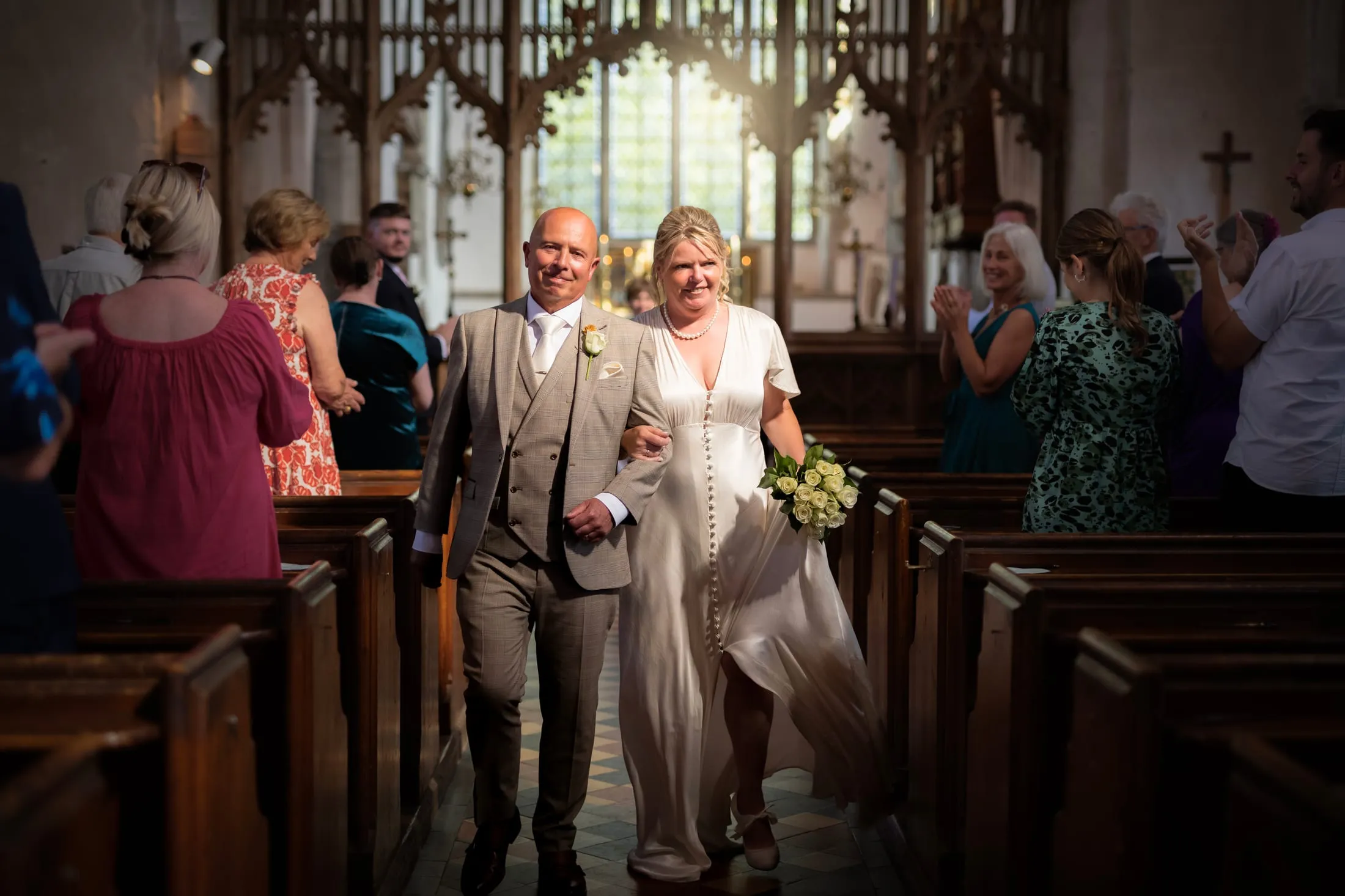 Bride and groom walking back down the aisle as guests applaud in a sunlit church